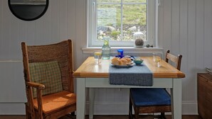 Un coin repas avec une table en bois, deux chaises, une fenêtre donnant sur un paysage verdoyant et un luminaire suspendu.