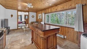 A wooden-paneled room with a large wooden table, a window with a view of trees, and a ceiling fan. - Charming Cabin on Dream Property (Pine)