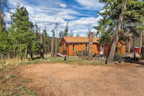A log cabin with a wooden deck, surrounded by pine trees. - Charming Cabin on Dream Property (Pine)