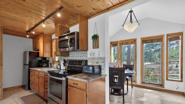 A modern kitchen with wooden cabinets, stainless steel appliances, and large windows offering a view of the outdoors. - Charming Cabin on Dream Property (Pine)