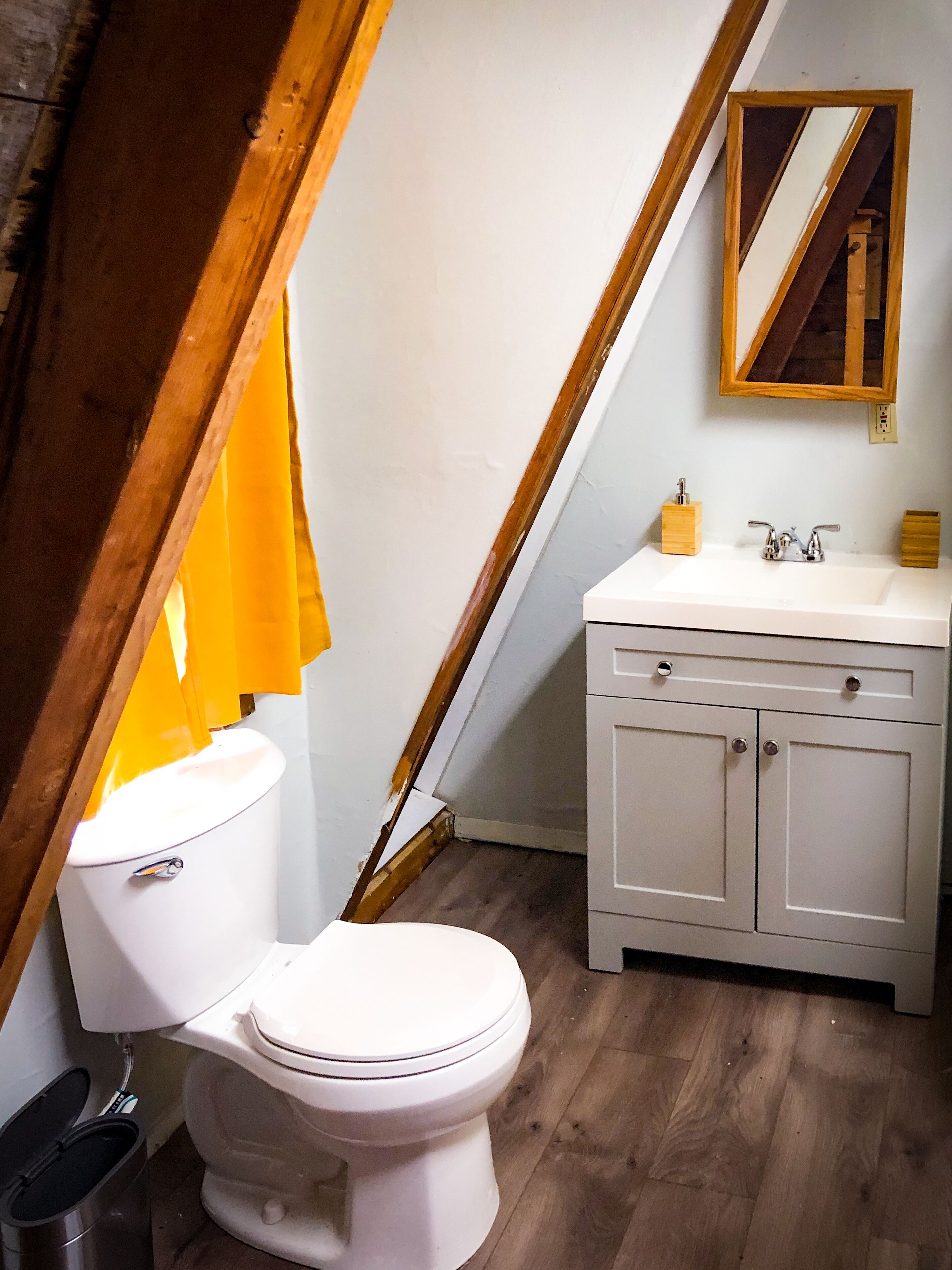 Ein Badezimmer mit Toilette, Holzboden und einem weißen Waschtisch mit Spiegel.