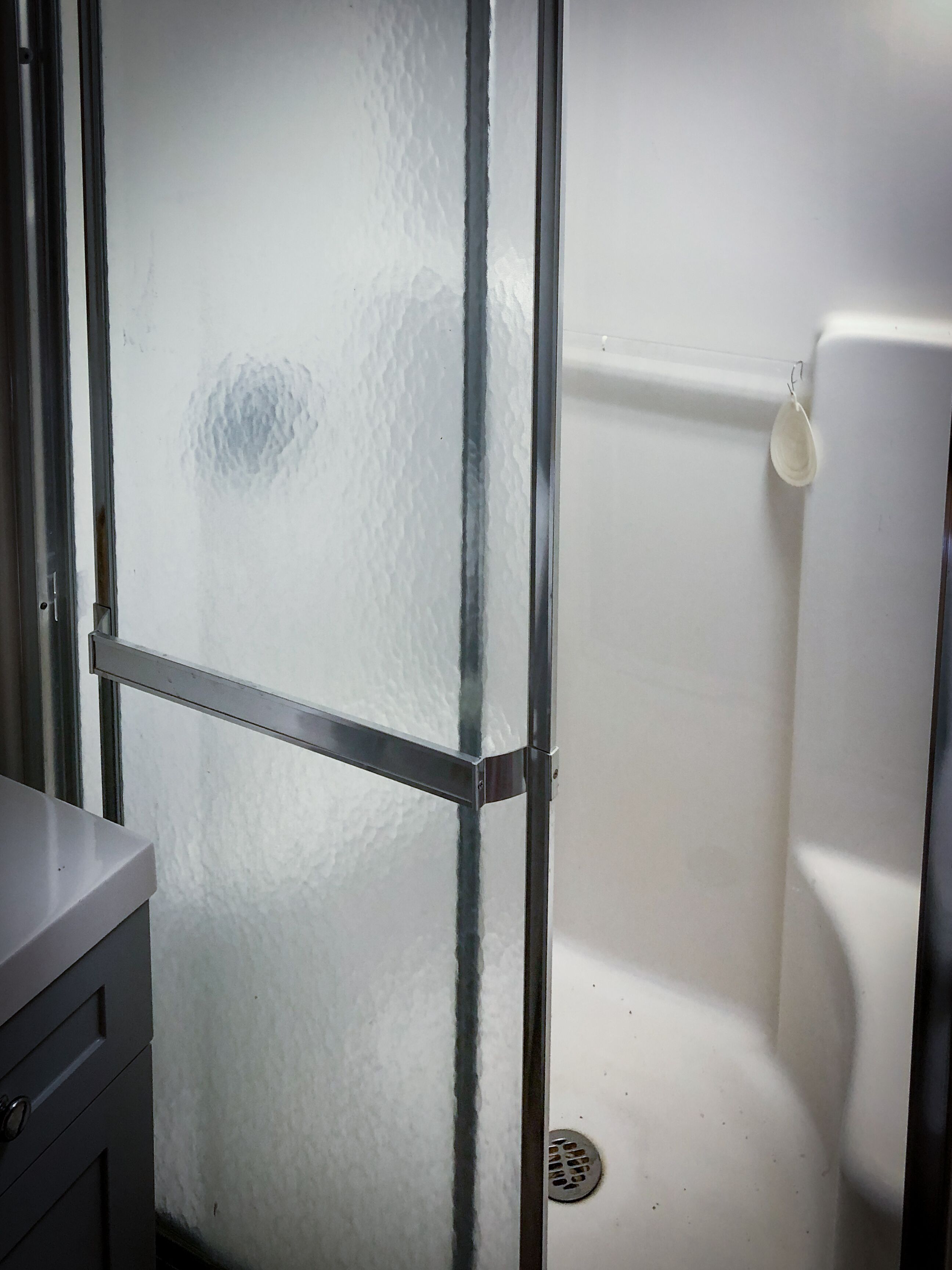 A bathroom with a frosted glass partition, a white bathtub, and a metal shower door.