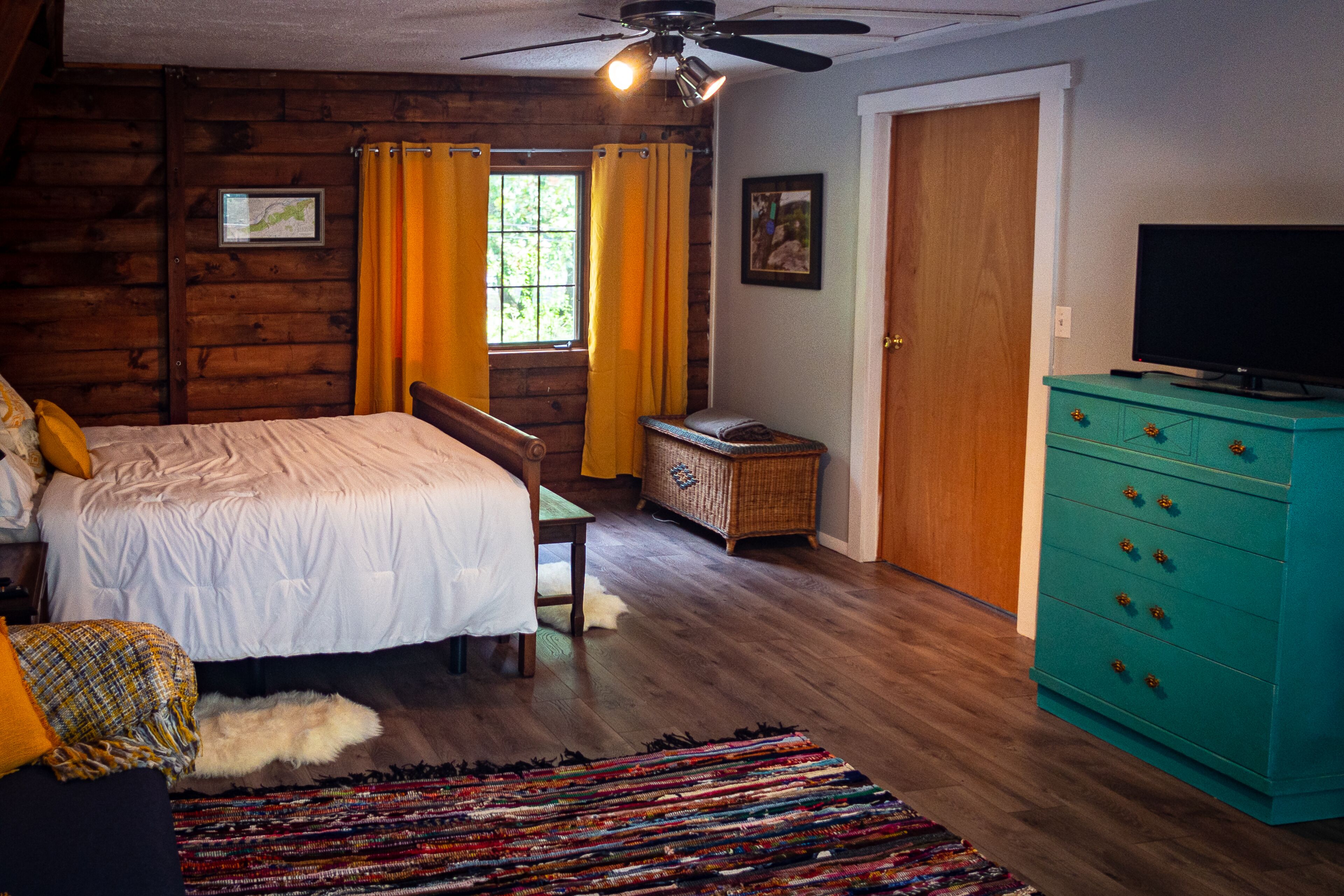 Un dormitorio con cama, televisor, cómoda y ventana con cortinas.