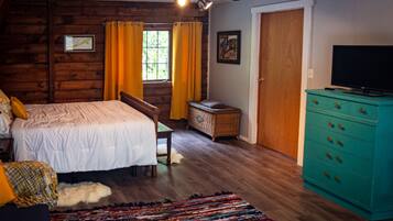 Un dormitorio con cama, televisor, cómoda y ventana con cortinas.