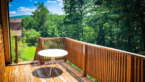 Une terrasse en bois avec une table ronde et des chaises, entourée d’une clôture en bois, offrant une vue sur un paysage verdoyant et luxuriant.