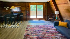 Un chalet confortable doté d’un coin repas, d’un canapé et d’une grande fenêtre offrant une vue sur la verdure.