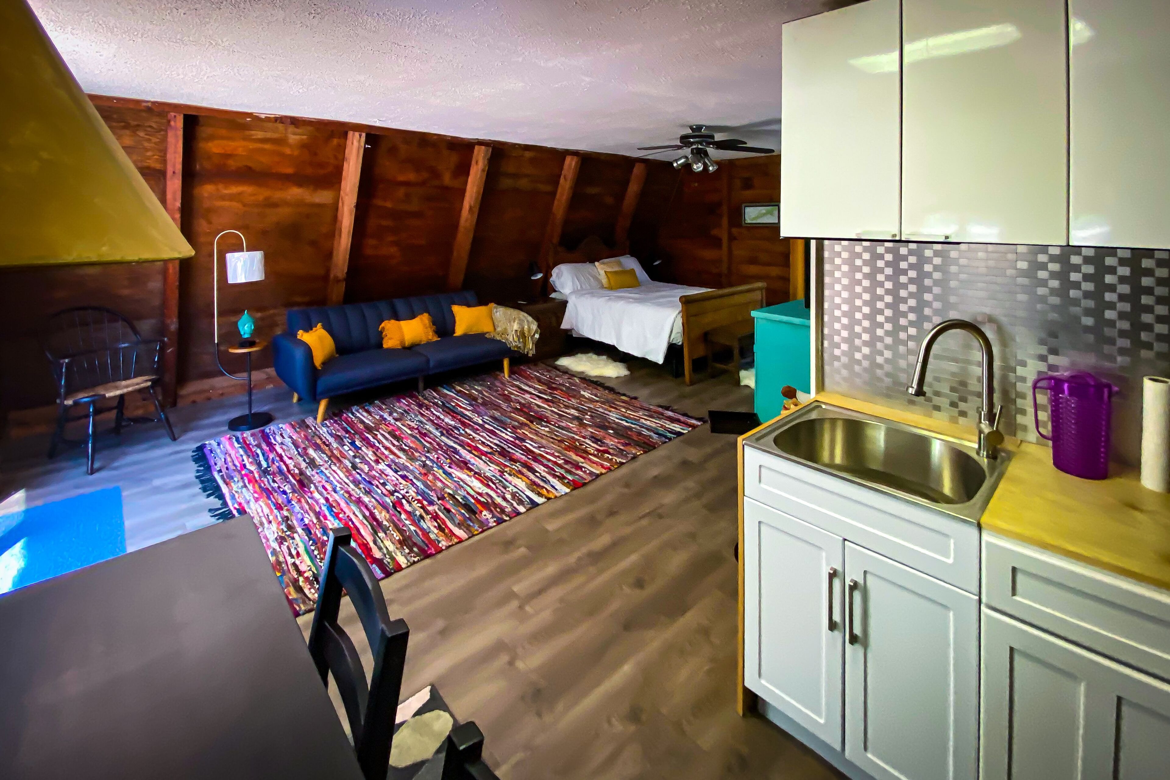 Una habitación pequeña y rústica con cama, sofá, mesa de comedor y espacio para cocinar.