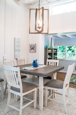 A dining area with a wooden table and white chairs, a hanging light fixture, and a wall with nautical-themed decor.