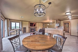 A spacious dining area with a round wooden table and metal chairs, a chandelier, and a kitchen in the background.