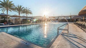 Ein Swimmingpool mit einer Tiefenmarkierung von 3 Fuß 6 Zoll, umgeben von Liegestühlen und Sonnenschirmen, mit Palmen und einem Gebäude im Hintergrund.