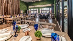 Ein Restaurant mit mehreren Esstischen, gedeckt mit blauem Glas, weißen Tellern und Kupfersalzstreuern.