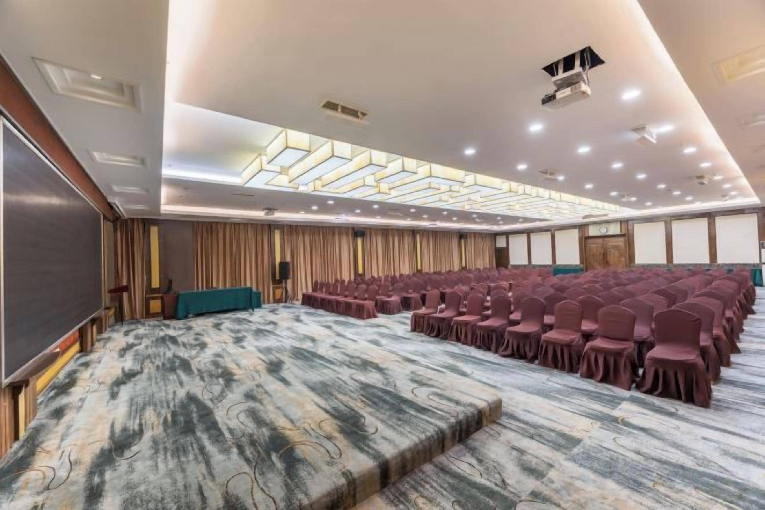 Un salón de conferencias con escenario, filas de sillas y suelo alfombrado.