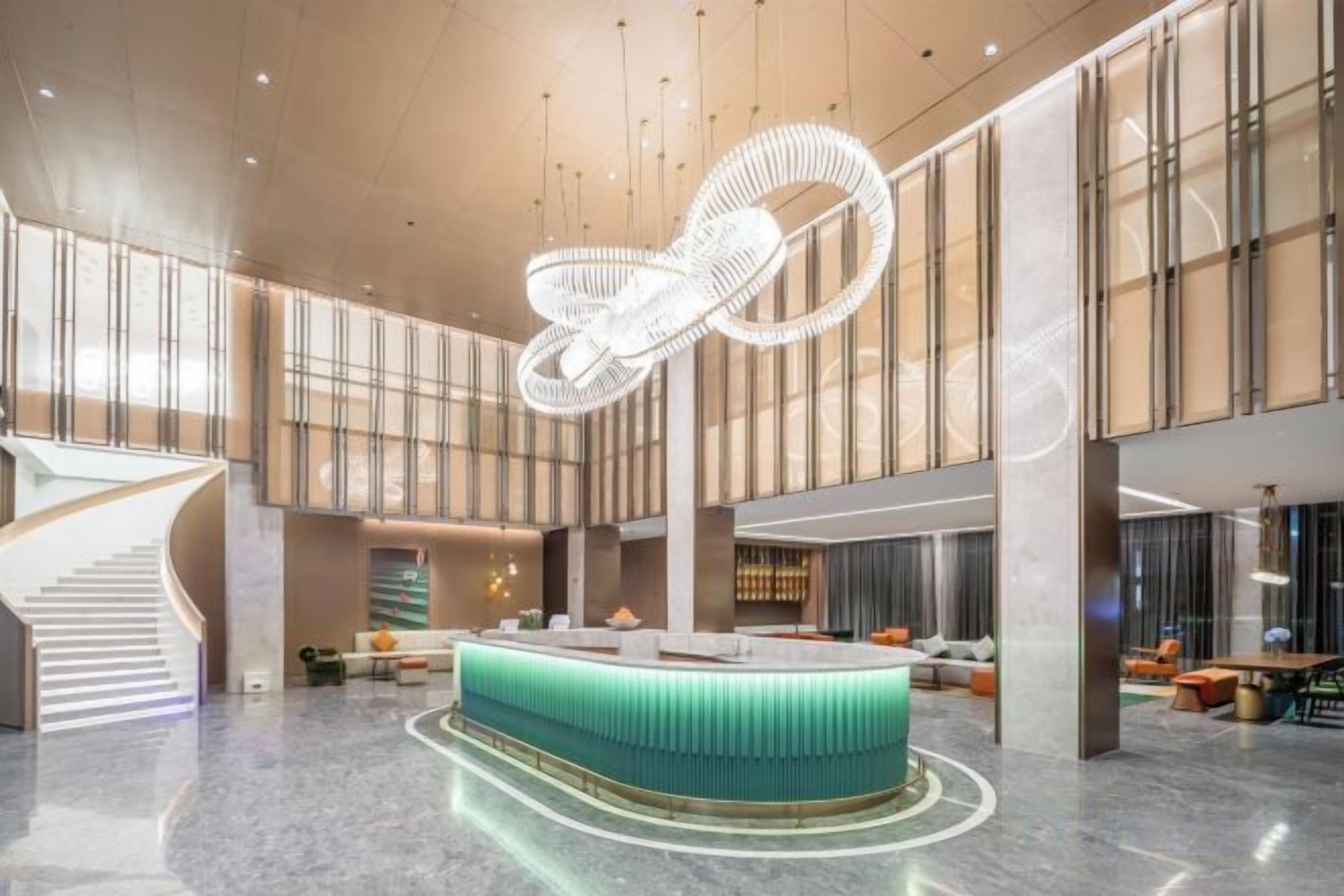 Un vestíbulo amplio con un mostrador de recepción central, una escalera y un moderno candelabro.