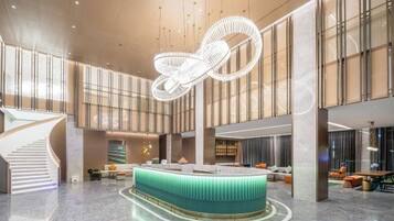 Un vestíbulo amplio con un mostrador de recepción central, una escalera y un moderno candelabro.