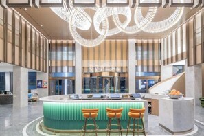 Een moderne lobby met een centraal gelegen bar, zitplaatsen en een trap.
