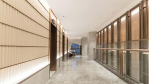 Un couloir d’hôtel moderne avec un sol en marbre, un lambris en bois sur le côté gauche et des rampes de protection en verre sur le côté droit.