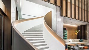 Un intérieur moderne avec un escalier à volutes, un espace salon avec des canapés et des tables, et un mur décoratif orné de panneaux verticaux.