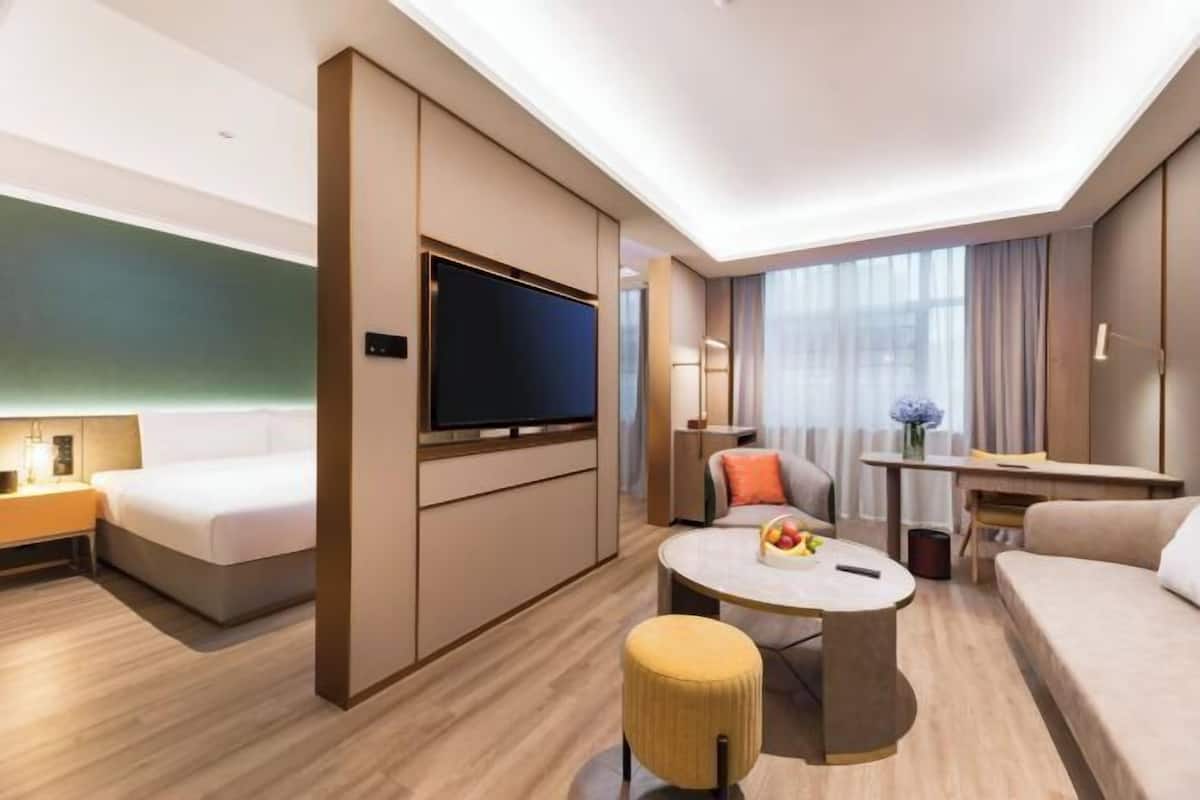 A modern hotel room with a bed, a flat-screen TV, a round coffee table, a sofa, and a small table with a vase of flowers.