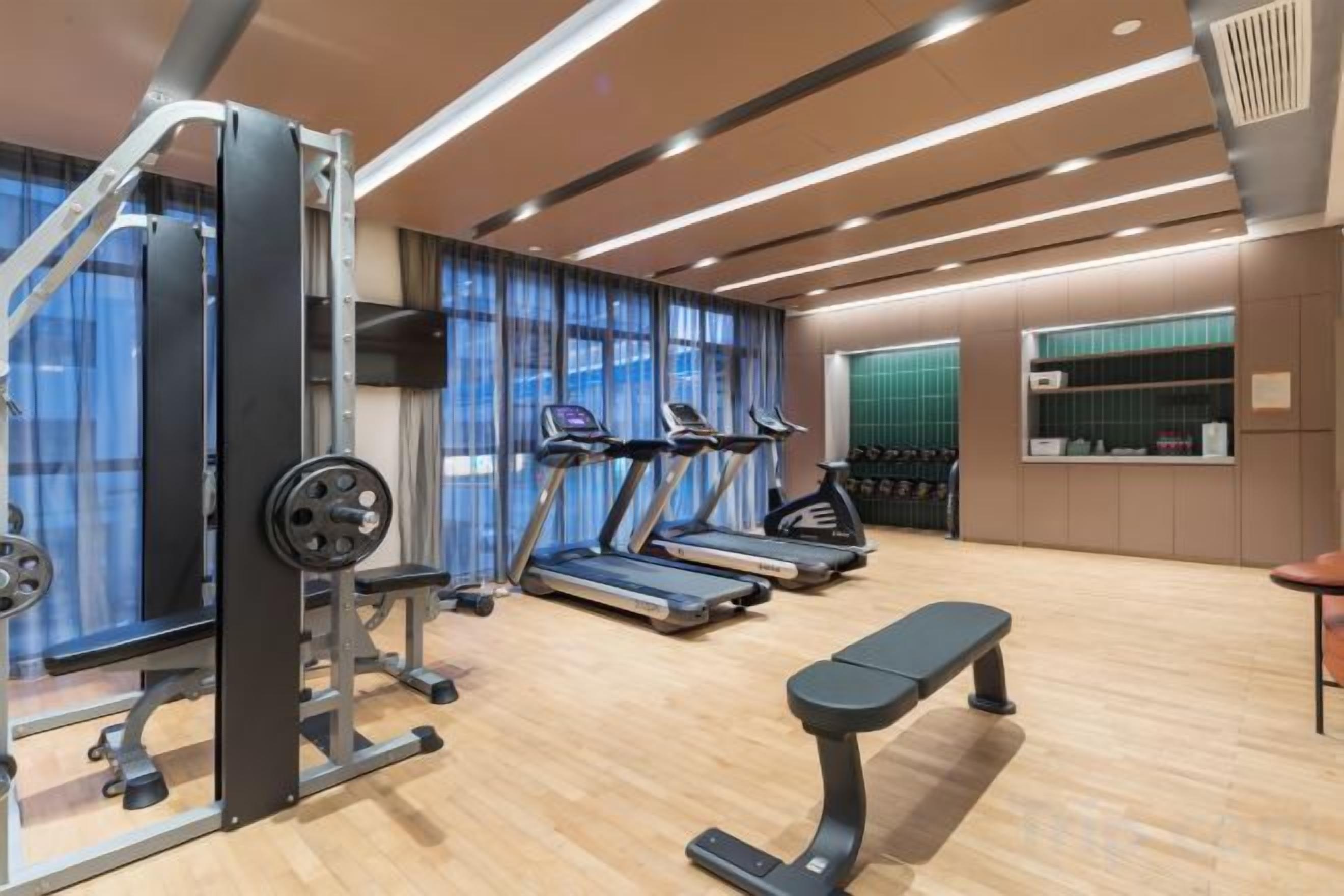 Academia com equipamentos de cardio, esteiras e um banco.