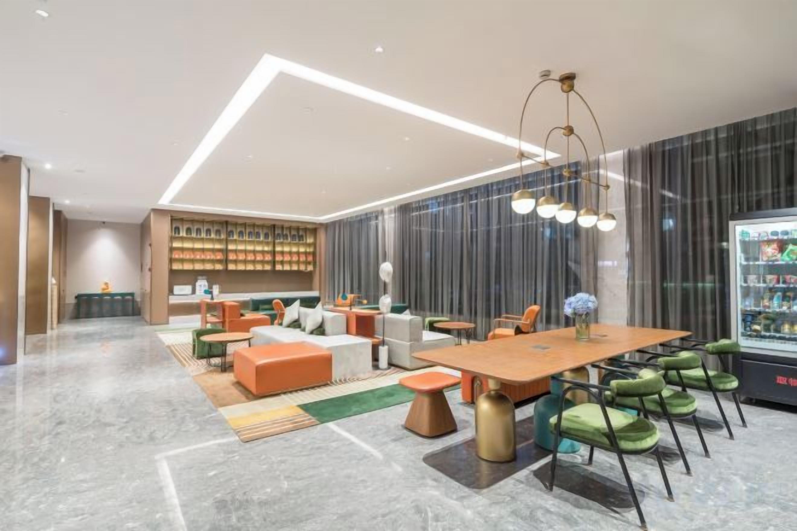 A modern hotel lobby with a dining area, seating arrangements, and a refrigerator.