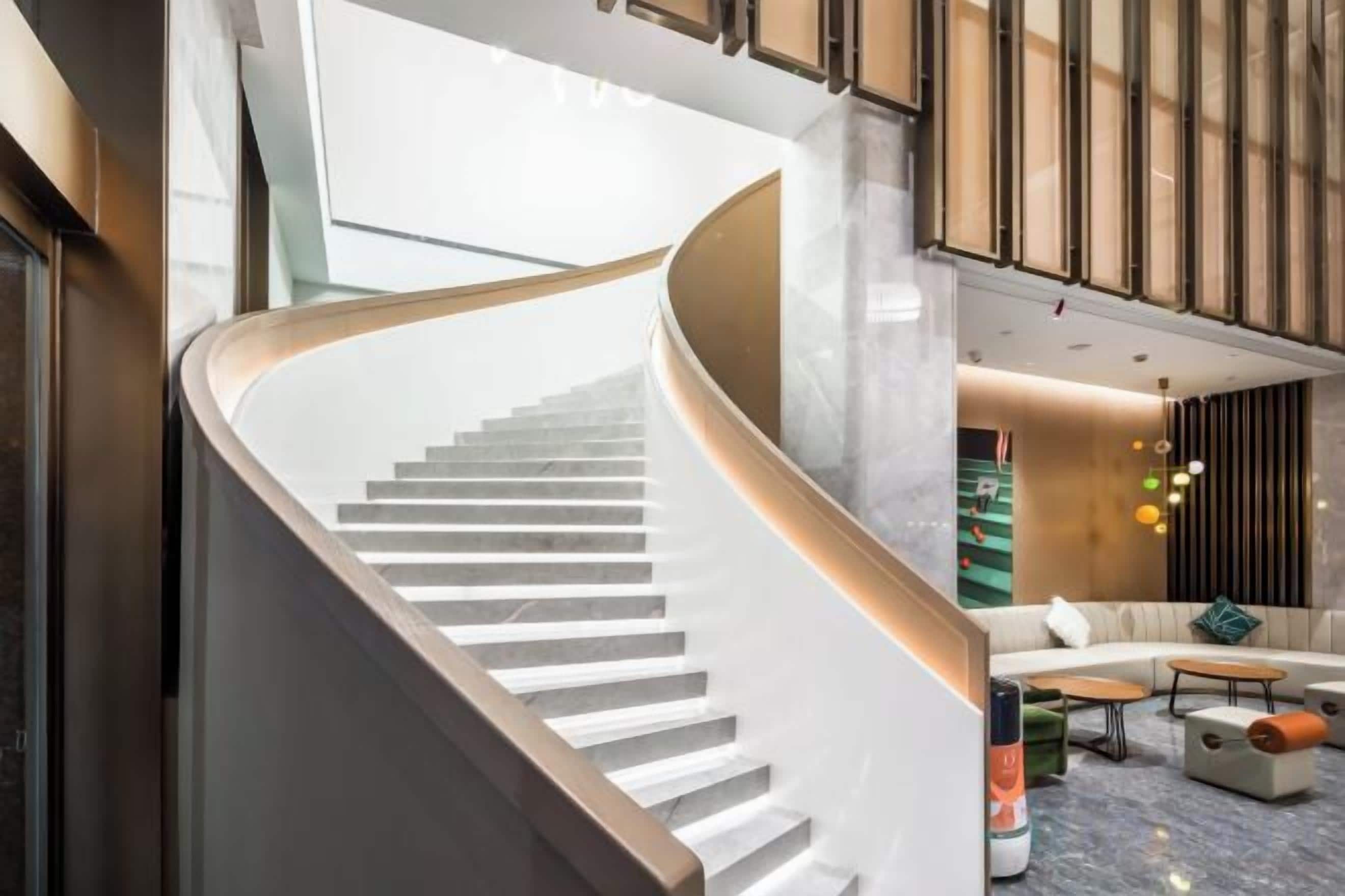 A modern interior with a curved staircase, a seating area with a sofa and coffee table, and a large window providing natural light.