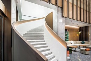A modern interior with a curved staircase, a seating area with a sofa and coffee table, and a large window providing natural light. - Hongyuan Hotel (Ningbo Railway Station) (Ningbo)