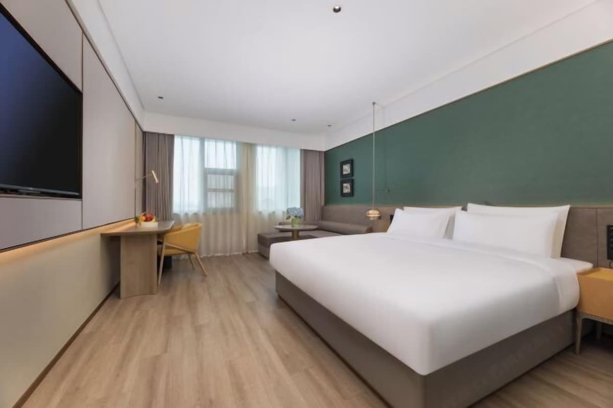 A modern hotel room with a large bed, a desk, a chair, and a television.