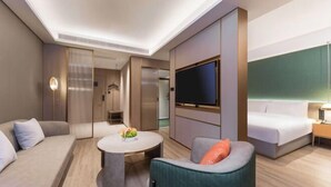 Une chambre d’hôtel moderne avec un canapé, une table basse ronde, un téléviseur fixé au mur, un lit et une table de chevet.