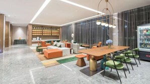 Un hall d’hôtel moderne doté d’un espace salon central, d’un bar et d’un réfrigérateur rempli de boissons.