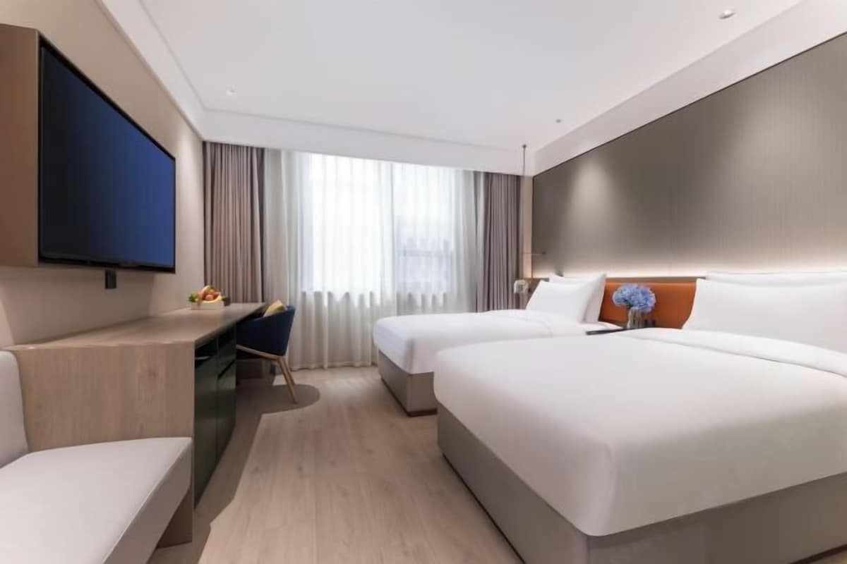 A modern hotel room with two beds, a desk, and a flat-screen TV.