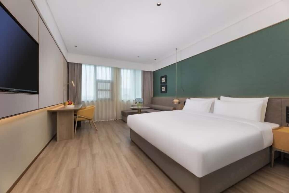 A hotel room with a large bed, a desk, a chair, a TV, and a window with curtains.
