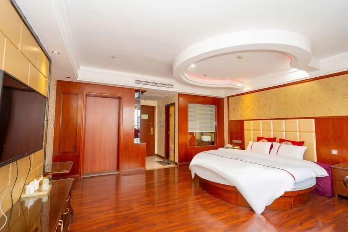 A hotel room with a large bed, a TV, a wooden floor, and a modern ceiling design.