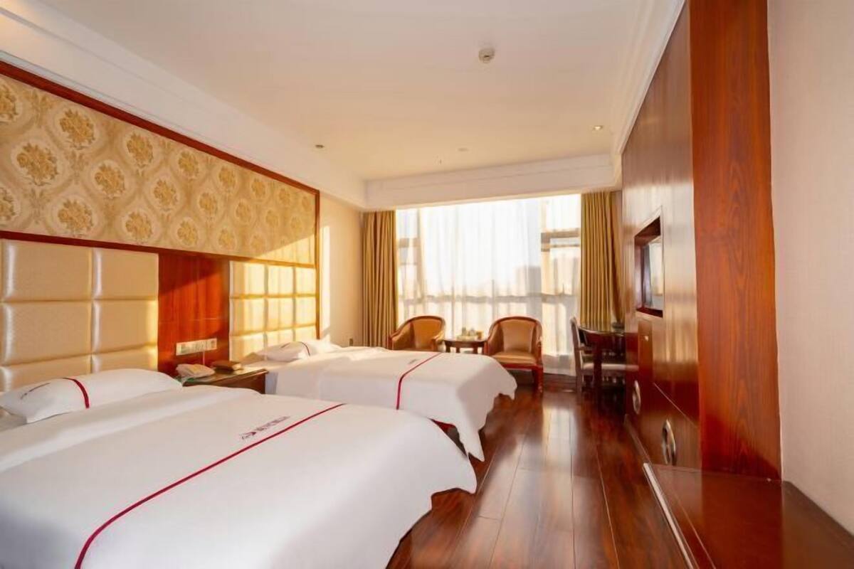 A hotel room with two beds, a wooden floor, a large window, and a television.