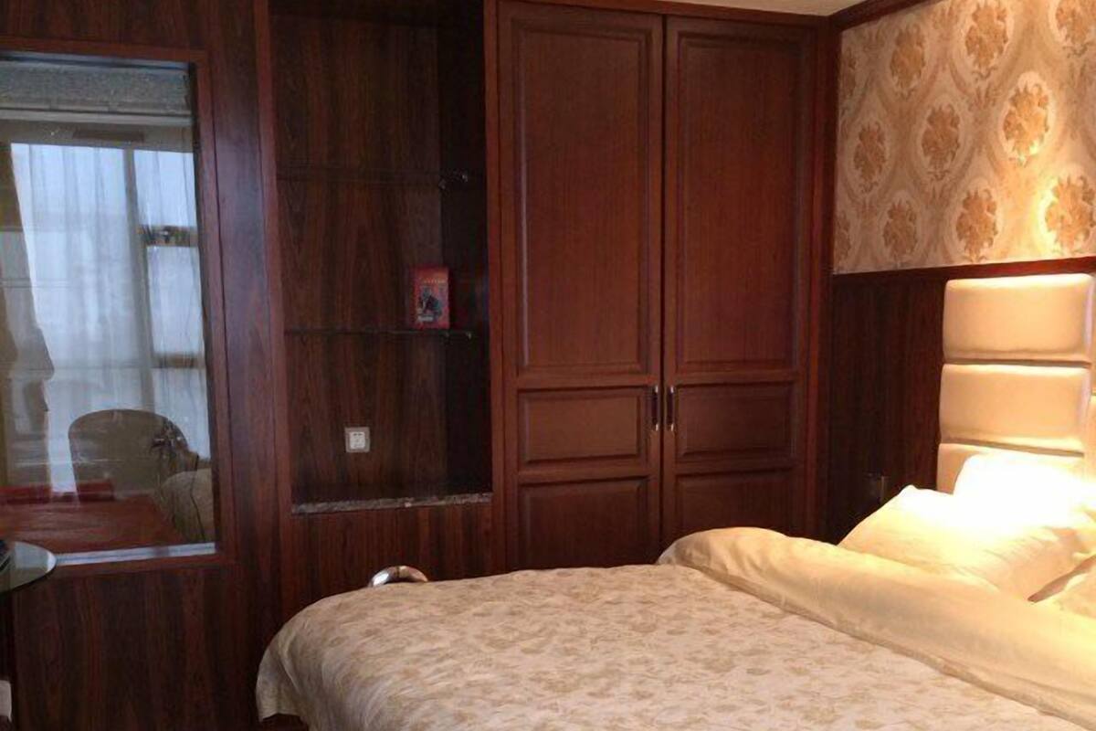 A bedroom with a bed, a wooden wardrobe, a mirror, and a nightstand.