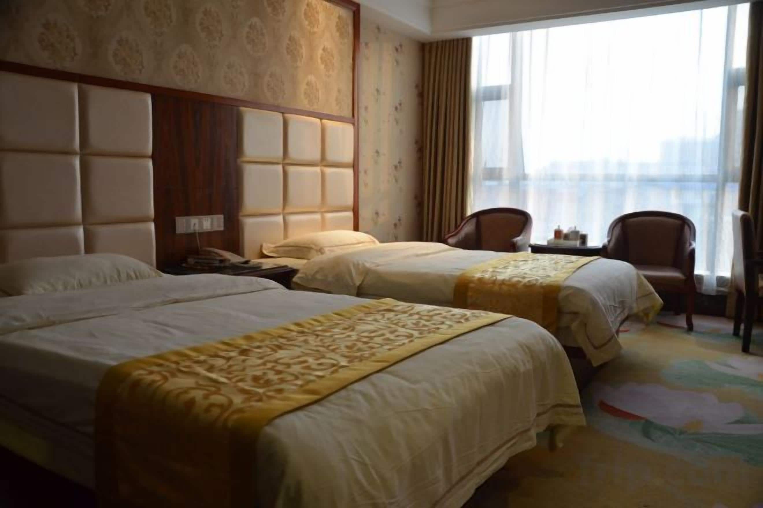A hotel room with two beds, a large window, and a view of the city.