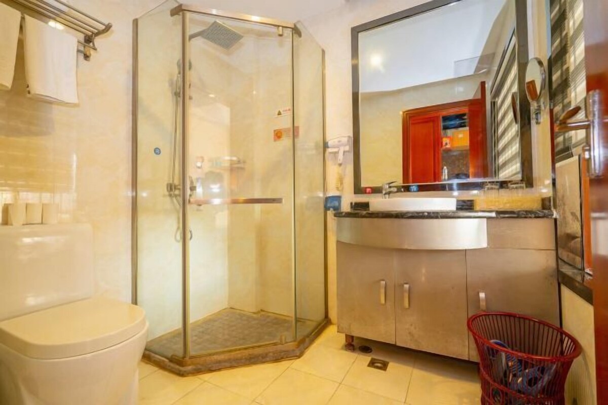 A bathroom with a glass-enclosed shower, a toilet, a sink with a mirror, and a red basket.