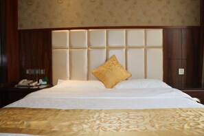 A hotel room with a large bed, a wooden headboard, a nightstand with a telephone, and a wall-mounted light. - Lihe Business Hotel (Huanggang)