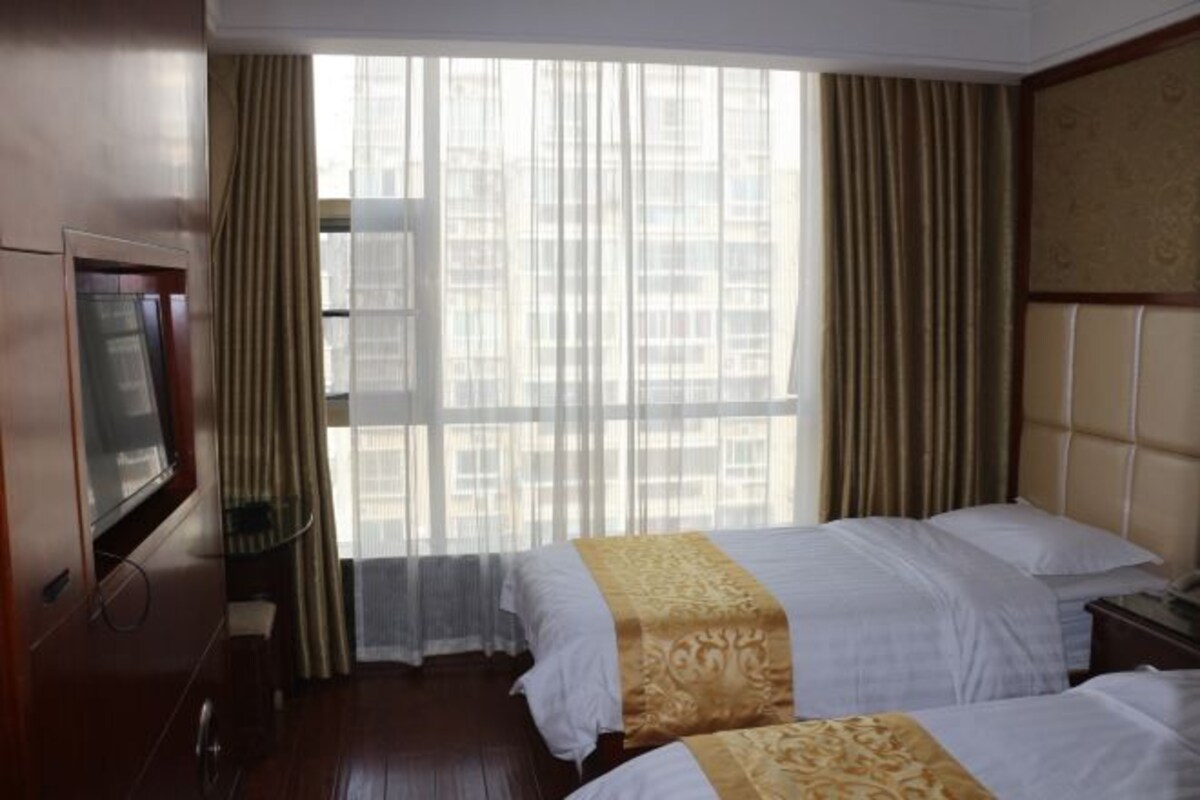 A hotel room with two beds, a television, and a large window with curtains.