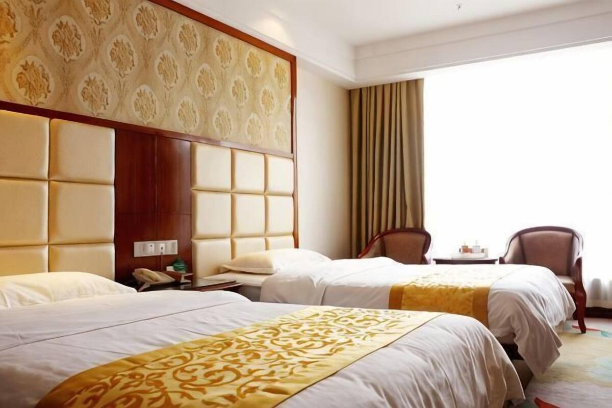A hotel room with two beds, a wooden headboard, a small table, and a chair.
