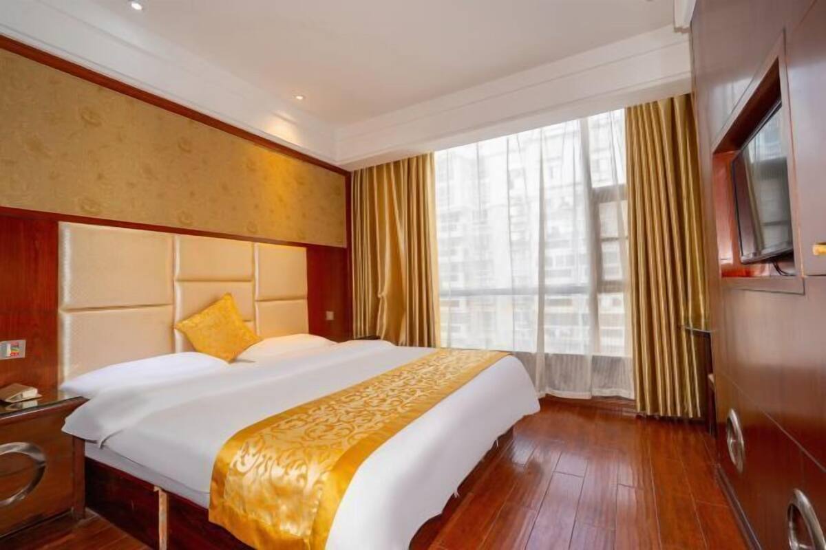 A hotel room with a large bed, a wooden headboard, a television, and a window with curtains.