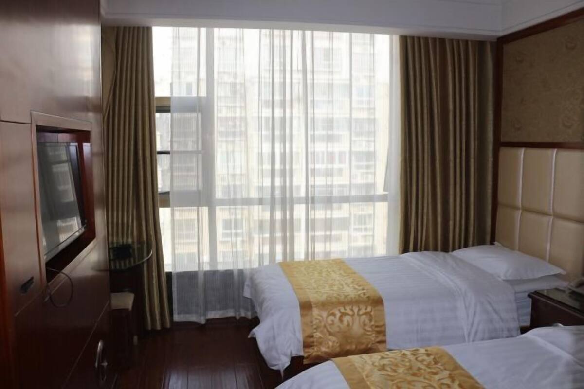 A hotel room with two beds, a television, and a large window with curtains.