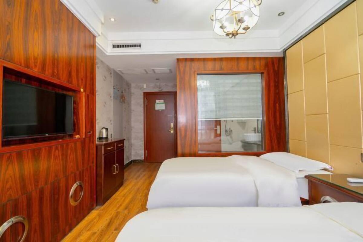 A hotel room with two beds, a TV, a minibar, and a bathroom visible through a glass door.