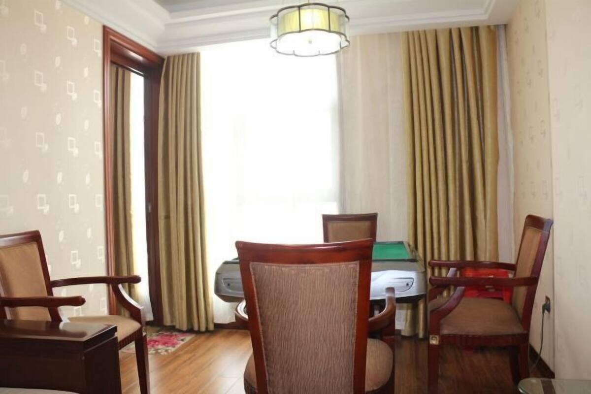 A room with a green pool table, four wooden chairs, a lamp, and a window with curtains.