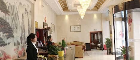 A hotel lobby with a reception desk, a chandelier, a large painting, and a seating area.