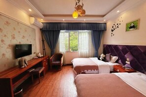 Habitación de hotel con televisión, escritorio, silla, dos camas, ventana con cortinas, lámpara en el techo y adornos en la pared.
