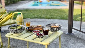 Taula amb menjar i begudes, piscina de fons i una cadira.