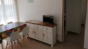 Ein Zimmer mit Esstisch, Stühlen, einem Fernseher auf einem Schrank, einem kleinen Bild an der Wand und einer Tür zu einem anderen Raum.