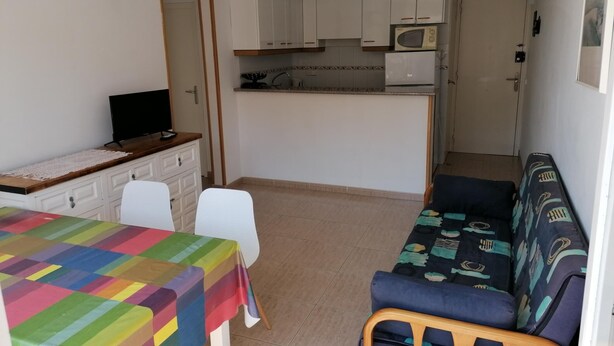 Ein kompakter Wohnraum mit Küchenzeile, einem Essbereich mit bunten Tischdecken und einer Couch mit gemusterten Bezügen.