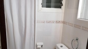 Ein kleines, sauberes Badezimmer mit Toilette, Waschbecken und einem Fenster über der Toilette.