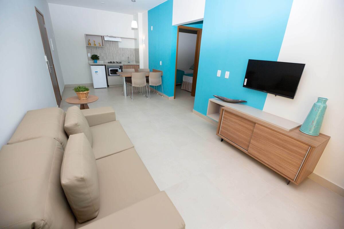 A modern living room with a beige sofa, a wooden TV stand, and a dining area with a small table and chairs.